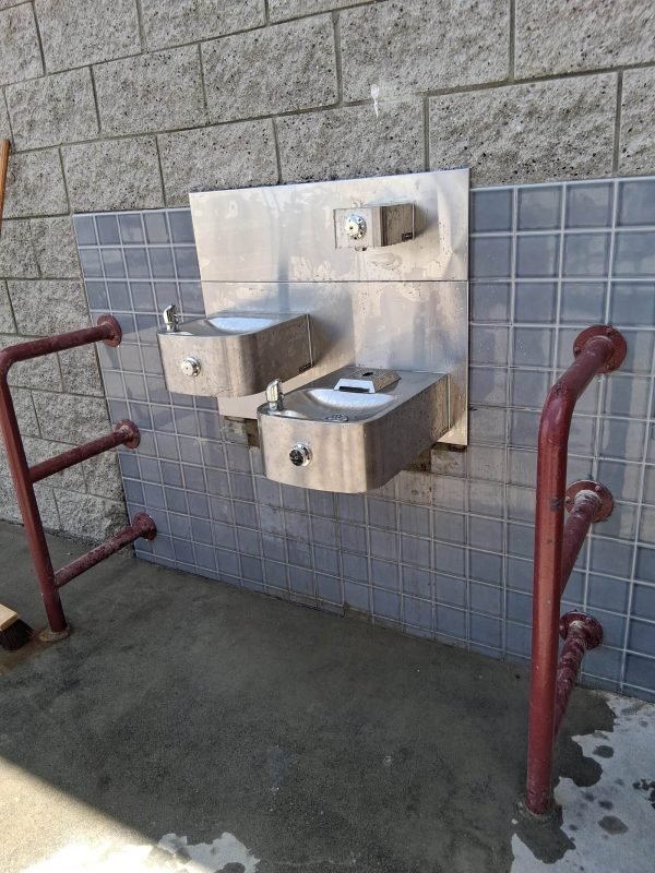 Two stainless steel drinking fountains with red metal railings outside a building.
